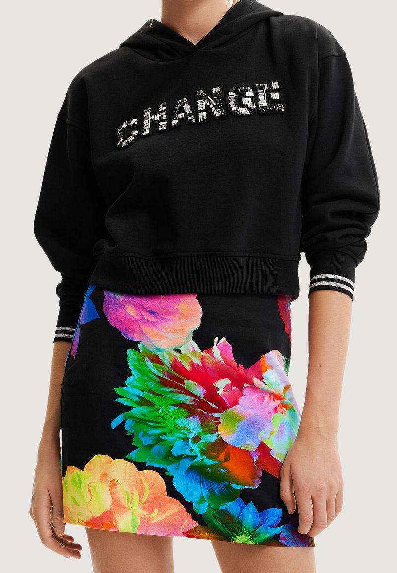 Czarna krótka bluza z kapturem z metalicznym napisem "CHANGE", zestawiona z dopasowaną mini spódniczką w żywe kwiatowe wzory na ciemnym tle.