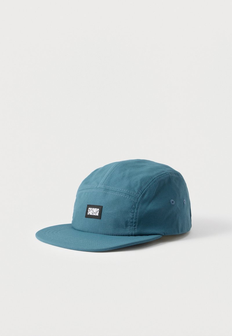 Καπέλο πέντε πάνελ σε τιρκουάζ χρώμα με επίπεδη γείσο και μαύρο σημείο με την επιγραφή «Columbia Sportswear» στο μπροστινό πάνελ πάνω σε λευκό φόντο.