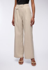 Pantaloni beige a gamba larga realizzati in tessuto testurizzato, con vita alta e dettaglio a fiocco frontale per un design aggiuntivo.