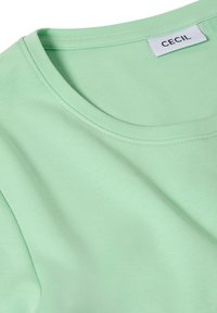 T-shirt en coton vert clair avec un col rond et une étiquette blanche portant la mention "CECIL" à l'intérieur du col arrière.