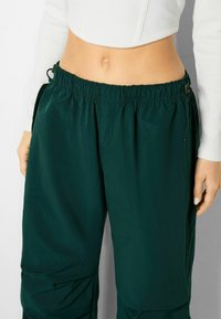 Mörkgröna, lätta byxor med resårmidja, dragsko och sidfickor. Slät textur med en avslappnad passform.