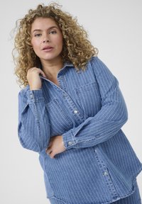Cămașă din denim de culoare albastru deschis, cu dungi verticale albe, mâneci lungi, două buzunare frontale și închidere cu butoni la față și pe mansete.