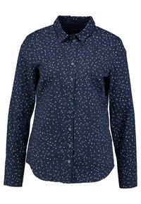 Chemise bleu marine à manches longues avec col boutonné, présentant un motif à points blancs épars, des boutons sur le devant et un ourlet droit.