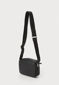 Borsa a tracolla rettangolare nera realizzata in materiale liscio, con chiusura a zip e tracolla regolabile con branding ripetuto.