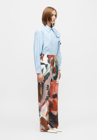 Φωτεινό γαλάζιο πουκάμισο με κουμπιά και λεπτομέρεια λουλουδιού στον γιακά, συνδυασμένο με παντελόνι καμπάνα με πολύχρωμο αφηρημένο σχέδιο. Παπούτσια σε ουδέτερο χρώμα.