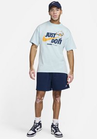 T-shirt en coton bleu clair avec un graphisme, shorts navy, chaussettes blanches et baskets navy. Présente un chef cartoon sur le t-shirt.