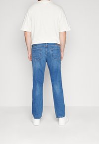 Ljusblå denimjeans med rak skärning, fem fickor och subtila sömnadsdetaljer, kombinerade med en krämfärgad t-shirt med kort ärm.