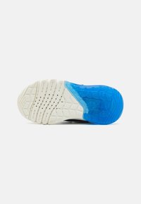 La semelle de la chaussure présente une base en caoutchouc texturé blanc avec une section translucide bleue, façonnée avec des rainures pour une meilleure adhérence.