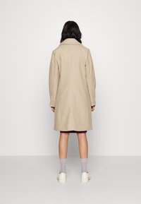 Abrigo de mezcla de lana beige con un ajuste relajado, cuello con muescas y mangas largas. Diseño de longitud media que termina por encima de las rodillas.