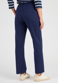 Pantaloni blu navy a vestibilità rilassata con vita elasticizzata, caratterizzati da una texture liscia e due tasche posteriori. Abbinati a sneakers beige.