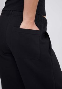 Schwarze Jogginghose mit seitlicher Tasche, elastischem Bund und glatter Textur, entworfen für Komfort und legere Freizeitkleidung.