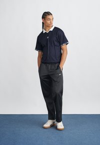 Polo din material cu model marin, cu guler alb, asortat cu pantaloni negri și adidași albi; prezintă detalii de marcă pe mâneci și talie.