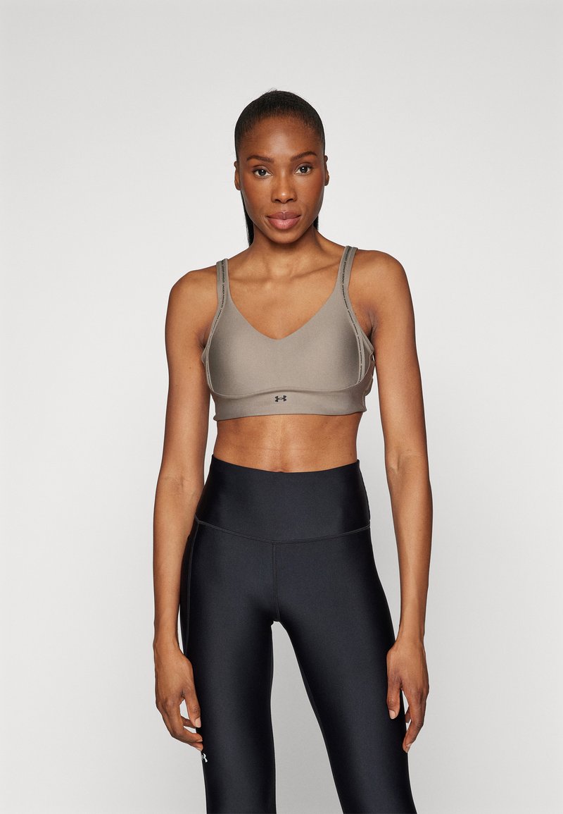 Sujetador deportivo gris con un diseño de escote en V y tirantes ajustables, combinado con leggings negros de cintura alta. Tejido suave y elástico, con una marca mínima.