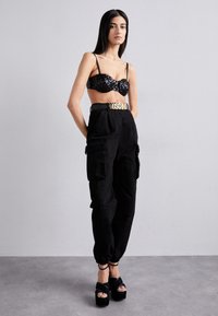 Fekete flitteres bralette vékony pántokkal, magasan szabott fekete cargo nadrággal, mely zsebekkel rendelkezik, és fekete platform cipőkkel bokapántokkal.