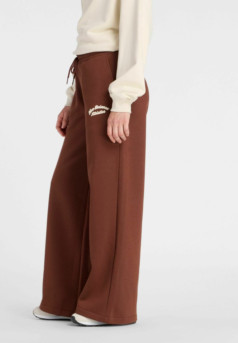 Bruine, wijde sweatpants met een elastische tailleband en trekkoord. Bevat witte geborduurde tekst en is gemaakt van zachte, gestructureerde stof.