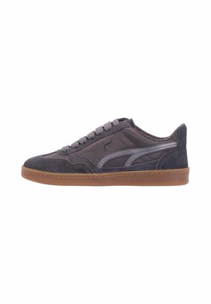 Zapatilla deportiva de ante y tela gris oscuro con suela marrón, franja lateral texturizada y cierre de cordones, mostrada de perfil.