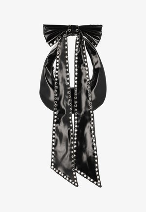 Černá kabelka z lakované kůže s velkou mašlí nahoře a dvěma dlouhými pásky připomínajícími stuhy. Okraje a otvory lemují stříbrné cvoky.