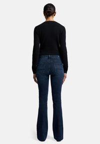 Mörkblå utsvängda jeans med en smidig textur, med en midjehöjd i normal höjd och bakfickor med lätt sömdetalj. Tiktat svart topp.