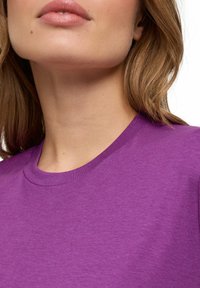 Paarse katoenen T-shirt met ronde hals, een gladde textuur en korte mouwen. De stof lijkt zacht met een subtiel gemêleerd patroon.