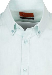 Lichtblauwe, knoopsluiting shirt van textuurstof, met een klassieke kraag en twee knopen aan de voorkant. Etiket zichtbaar binnen de kraag.