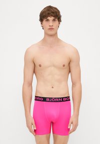 Gaiši rozā bokseri, kas izgatavoti no gludas materiāla, ar melnu jostu, kurā ar bieziem rozā burtiem ir printēts "BJÖRN BORG".