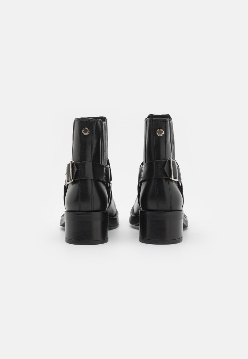 Schwarze Leder-Ankle-Boots mit glatter Oberfläche, ausgestattet mit einem Schnallenriemen und einem markanten Absatz. Das Design umfasst vertikale Nähte und metalliche Akzente.