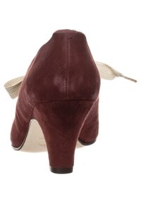 Scarpa con tacco alto in suede borgogna, dalla texture liscia, con un tacco piccolo e un dettaglio in nastro beige sul retro.