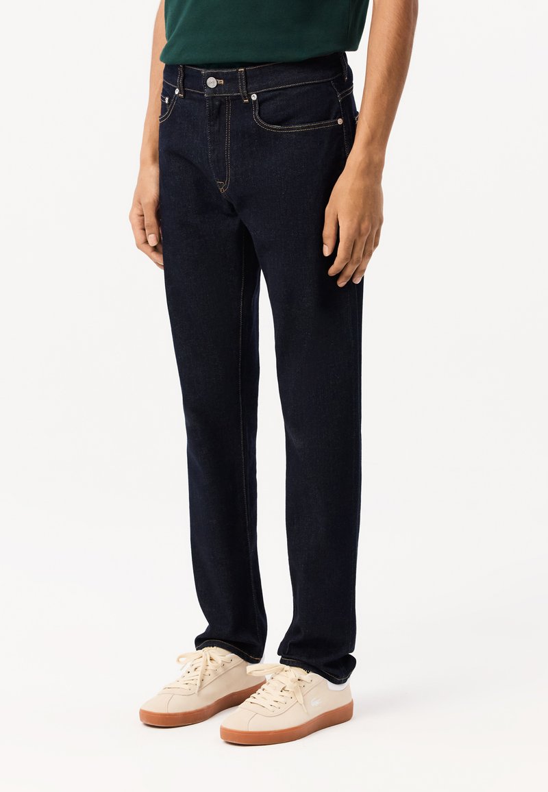 Jeans de mezclilla azul oscuro con ajuste recto, que presentan costuras de cobre, bolsillos delanteros y un cierre clásico de botón.