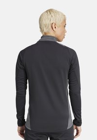 T-shirt de sport à manches longues avec un corps gris foncé et des accents gris clair, fabriqué en tissu lisse et extensible, conçu pour le sport.