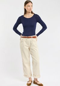 Haut en tricot à manches longues bleu marine associé à un pantalon beige clair à revers et des ballerines en daim marron, complété par une ceinture marron. Design simple et décontracté.