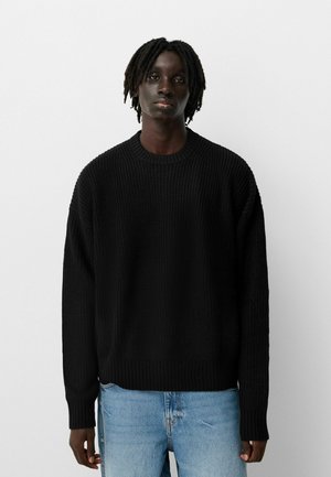 Black knitted sweater with a round neckline, ribbed cuffs, and a relaxed fit, paired with light blue denim jeans.