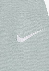 Šviesiai žaliu megztu audiniu puošia baltas siuvinėtas Nike swoosh logotipas, pabr�ėžiantis tekstūrą ir prekės ženklo detales.