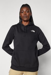Black hooded sweatshirt made of soft fabric, featuring a front pocket and a small white logo on the left chest area.