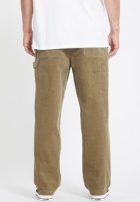 Pantalon en velours côtelé vert olive avec une coupe décontractée, comportant deux poches arrière et une poche latérale, complété par des baskets blanches.