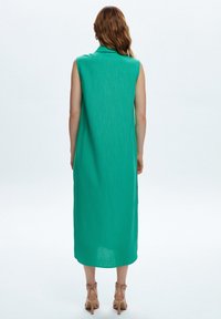 Abito lungo senza maniche di colore verde con colletto, realizzato in tessuto leggero. Presenta una silhouette dritta e una texture morbida.