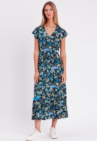 Robe portefeuille florale à fond noir, avec des motifs floraux bleus et verts, des manches courtes volantées et un ourlet en couches, portée avec des baskets blanches.