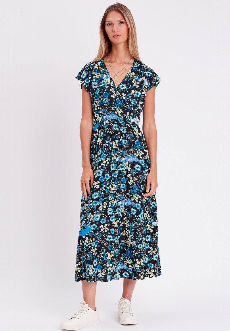 Robe portefeuille florale à fond noir, avec des motifs floraux bleus et verts, des manches courtes volantées et un ourlet en couches, portée avec des baskets blanches.