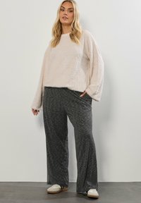 Jasnoróżowy włochaty sweter z długimi rękawami w połączeniu z ciemnoszarymi, wzorzystymi szerokimi spodniami; model nosi białe buty wsuwane.