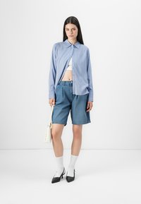 Camisa azul e branca de riscas, cortada sobre uma blusa branca, combinada com calções de ganga largos, meias brancas e sapatos de salto pretos.