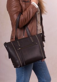 Black leather tote bag with a structured shape, featuring a front zipper pocket, contrasting stitching, and long handles.