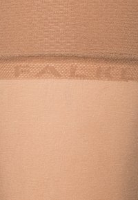 Tan nylon strømpebukser med en glat finish og en gennemsigtig kant, der viser mærket "Falke" i et subtilt, tonet mønster.