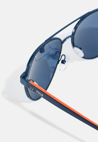 Óculos de sol navy com lentes escuras, armação fina em metal e destaque laranja nas hastes, apresentando almofadas de nariz ajustáveis e marca "POLO".