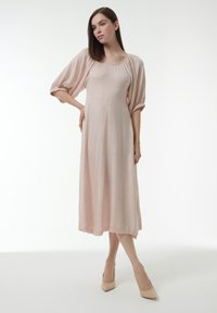 Helles rosa, knielanges Kleid mit lockerer Passform, Puff�ärmeln und gerafftem Ausschnitt. Das Material wirkt weich und leicht strukturiert.