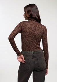 Maglione a maniche lunghe marrone con collo alto, caratterizzato da un design a stampa leopardata, abbinato a jeans in denim scuri a vita alta con tasche posteriori.
