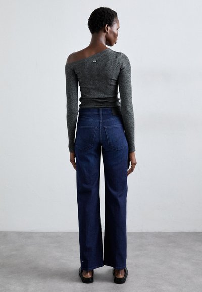Jeans de pierna ancha de color azul oscuro combinados con un suéter ajustado gris sin mangas de canalé. Detalles notables incluyen costuras mínimas y una cinturilla estándar.