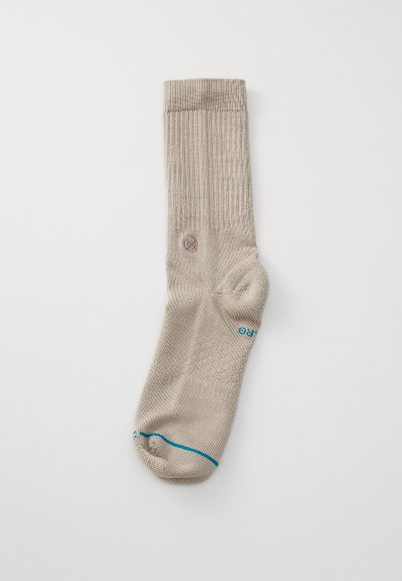 Beige ribbed sock with a cushioned toe, featuring a teal accent at the base and a small circular logo near the ankle.