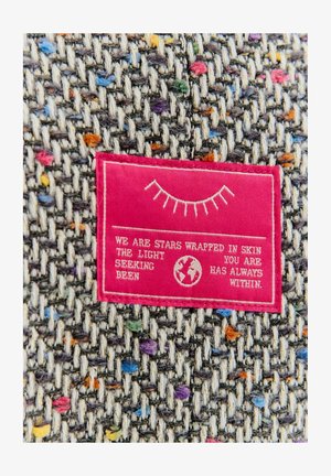 Tkanina z szarym wzorem tkanym, przerywanym kolorowymi plamkami. Różowa metka materiałowa z białym tekstem i grafiką kuli ziemskiej.