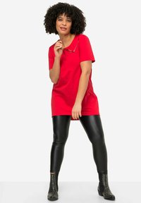 Tunic rossa in cotone con maniche corte, abbinata a leggings neri in finta pelle e stivali neri alla caviglia con borchie argentate.