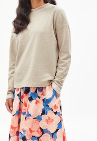 Světlé béžové mikinové tričko s nízkými ramínky, doplněné květinovou sukní s velkými růžovými a modrými květy na tmavém pozadí.