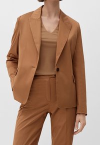 Brun skræddersyet blazer med notch lapels, enkel knaplukning og frontlommer; båret over en matchende brun top og bukser. Glat stof.